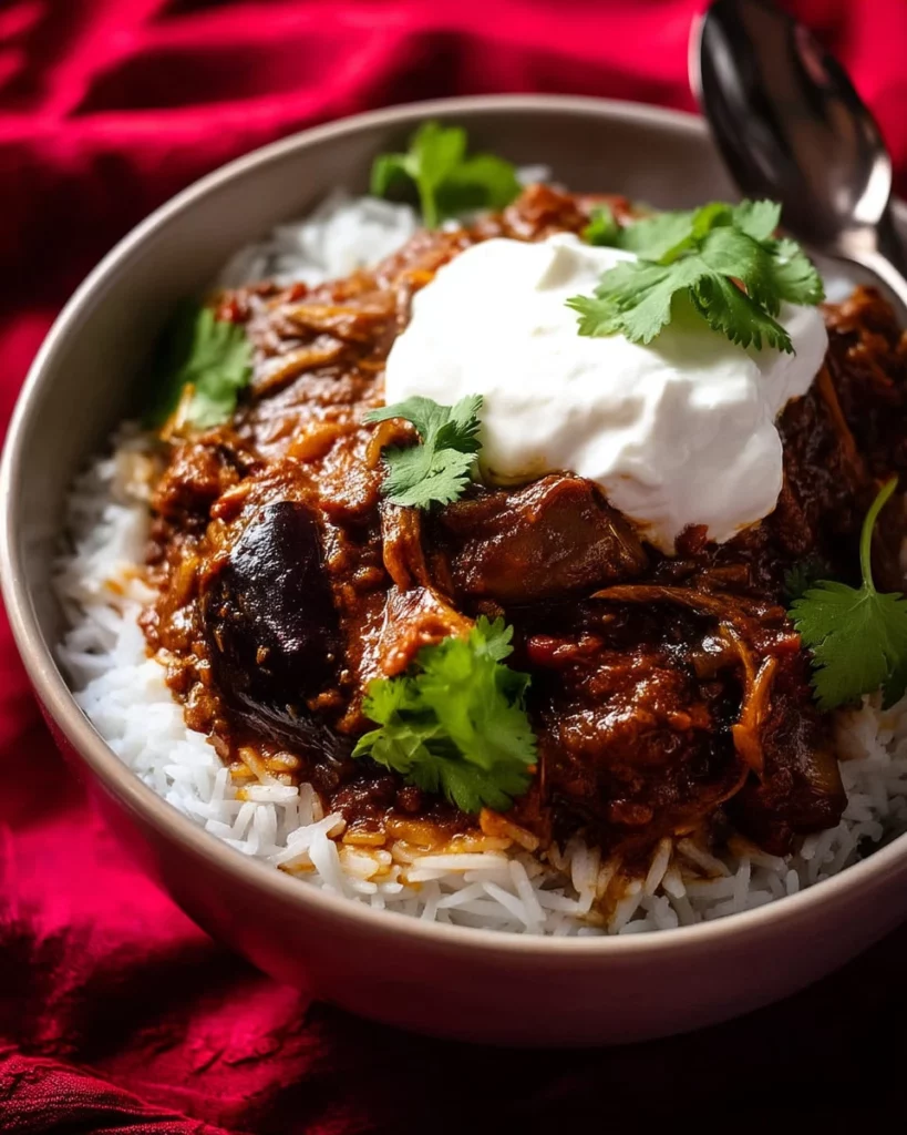 Bowls of delicious eggplant curry served with rice and garnish.